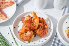 three white plates filled with shrimp and bacon on top of a checkered table cloth