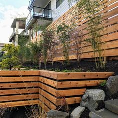 a wooden fence next to some rocks and plants on the side of a building with a balcony in the background