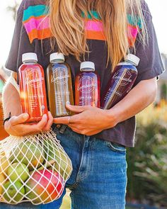 a woman holding four bottles of juice in her hands