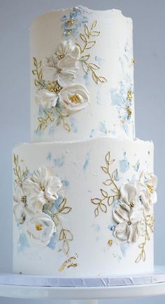 a three tiered wedding cake with white and blue flowers on the top, sitting on a stand