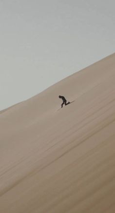 a person riding a snowboard down the side of a sand dune in the desert