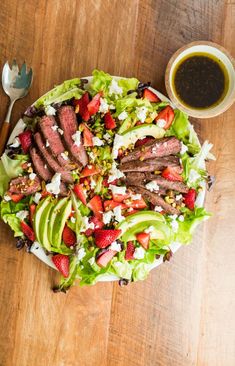 a salad with steak, lettuce and strawberries on it next to a cup of coffee