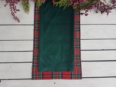 a green and red plaid table runner on a white wooden surface with flowers in the background