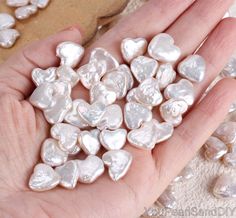 a person's hand holding several heart shaped pearls in their palm, with other hearts scattered around them