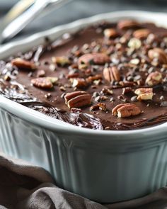 a close up of a cake in a pan with pecans and chocolate frosting