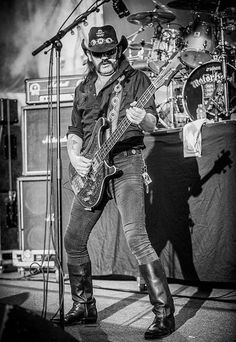 black and white photograph of a man playing guitar on stage with microphones in the background