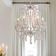 a chandelier hanging from the ceiling in front of a window with curtains and candles