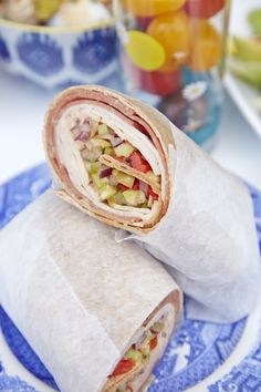 two wraps are sitting on a plate with fruit in the background and one wrap has been cut open