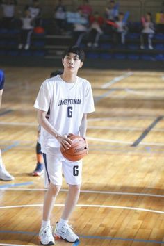 a young man holding a basketball on top of a wooden court with people watching from the sidelines