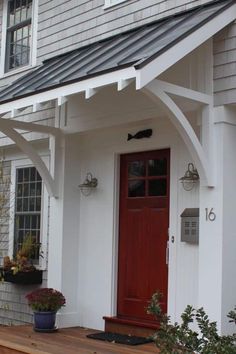 a white house with a red door and some plants on the front porch, next to it is a planter filled with flowers