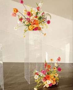 three clear vases with flowers in them sitting on a marble floor next to each other