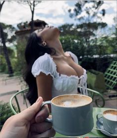 a person holding a cup of coffee in front of a woman with her eyes closed