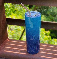 a blue cup sitting on top of a wooden bench next to a metal straw holder