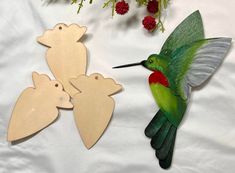 two wooden cutouts of birds and a hummingbird on a white sheet with red flowers