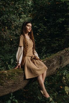 a woman sitting on top of a tree branch in the middle of a forest wearing a brown dress