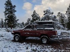 a red pick up truck parked on top of a snow covered field with trees in the background