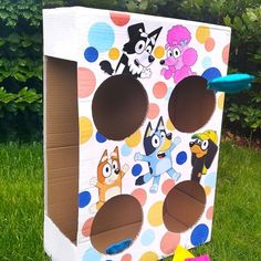 a cardboard box with cutouts of cartoon characters on it sitting in the grass next to a frisbee