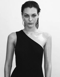 black and white photograph of a woman in a one - shoulder dress with large hoop earrings