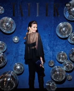 a woman is standing in front of some disco balls and looking at the camera with her hand on her hip