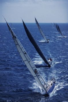 several sailboats are sailing in the open ocean water, one is blue and white