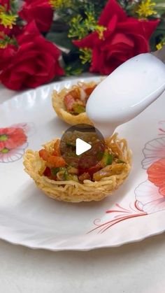 two small pastries on a white plate with red flowers in the backgroud