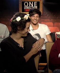 two men sitting next to each other in front of a sign that says one direction