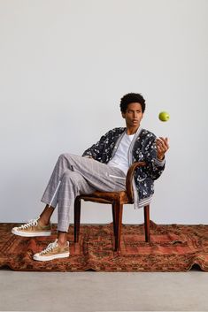 a man is sitting on a chair with an apple in his hand and tennis ball in his other hand