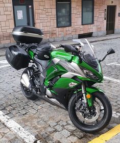 a green and silver motorcycle parked on the side of a road next to a building