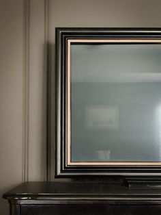 a mirror sitting on top of a wooden table next to a wall with a lamp