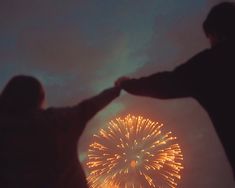 two people are holding hands with fireworks in the sky behind them and one person has their arms around the other