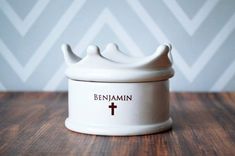 a white ceramic container with a crown on it sitting on top of a wooden table