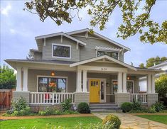 a gray house with white trim and yellow door on the front porch is surrounded by greenery