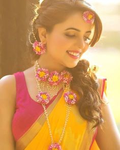 a woman in yellow and pink sari with flowers on her head, smiling at the camera