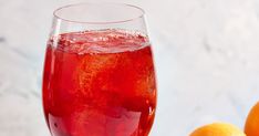 a glass filled with red liquid next to oranges on a white tablecloth and marble background