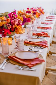 the table is set with plates, silverware and vases filled with colorful flowers