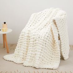 a white crocheted blanket sitting on top of a floor next to a table