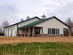 a large white building with green roofing and two doors on the front, surrounded by tall grass