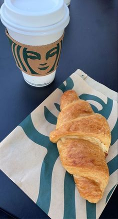 a croissant sitting on top of a napkin next to a cup of coffee