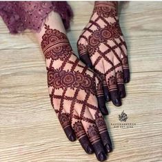 two hands with henna tattoos on them sitting on a wooden floor next to each other