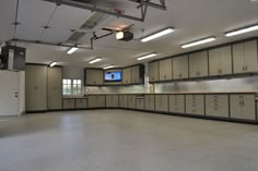 an empty garage with lots of cabinets and lights on the ceiling, in front of a flat screen tv