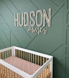 a baby crib in front of a green wall with the name hudson james on it