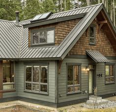 a house in the woods with metal roofing and wood shingles on the windows