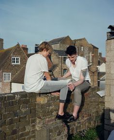 two young men sitting on top of a brick wall