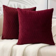 two red pillows sitting on top of a couch next to a white pillow case with palm leaves in the background