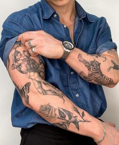 a man with tattoos on his arm and wrist is posing for the camera while wearing a blue shirt