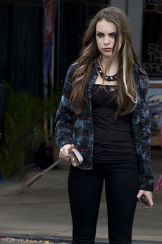 a woman with long hair and black pants holding a knife in her hand while standing on the street