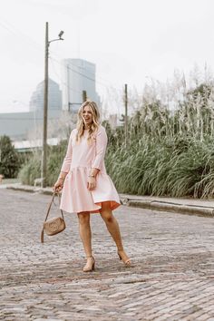 a woman in a pink dress is walking down the street with her purse and handbag