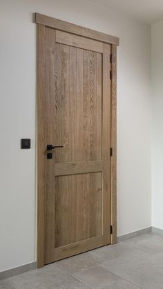 an empty room with a wooden door and tile flooring on the ground, in front of a white wall