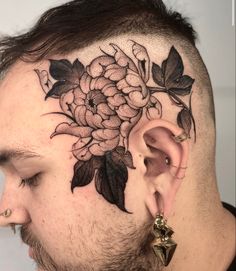 a man with a flower tattoo on his head and behind the ear is an ear piercing