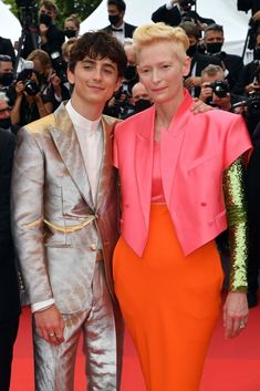 two people standing next to each other on a red carpet with cameras in the background